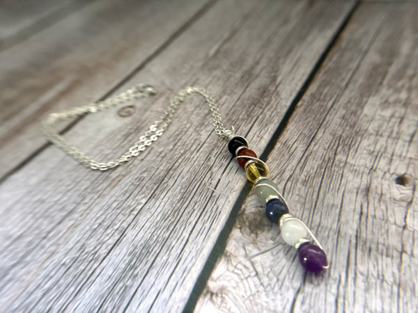 Seven-stone chakra necklace with silver-coloured wire wrapping on a rustic wooden background.