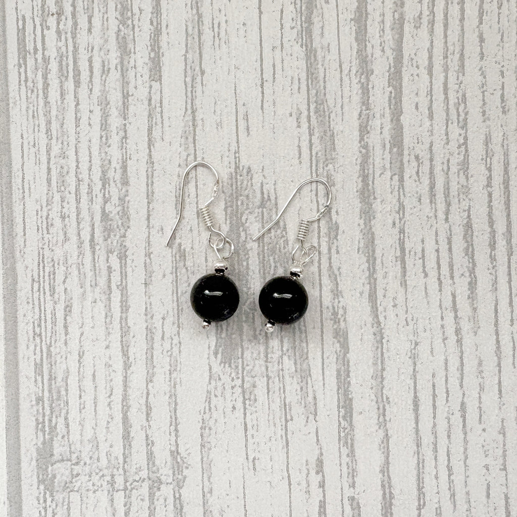 A pair of black bead drop earrings with silver fishhook wires, displayed against a light gray wood-grain background.