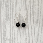 A pair of black bead drop earrings with silver fishhook wires, displayed against a light gray wood-grain background.