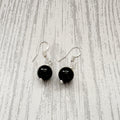 A pair of dangle earrings with round black beads and silver fishhook wires, displayed on a light gray wood-grain surface.