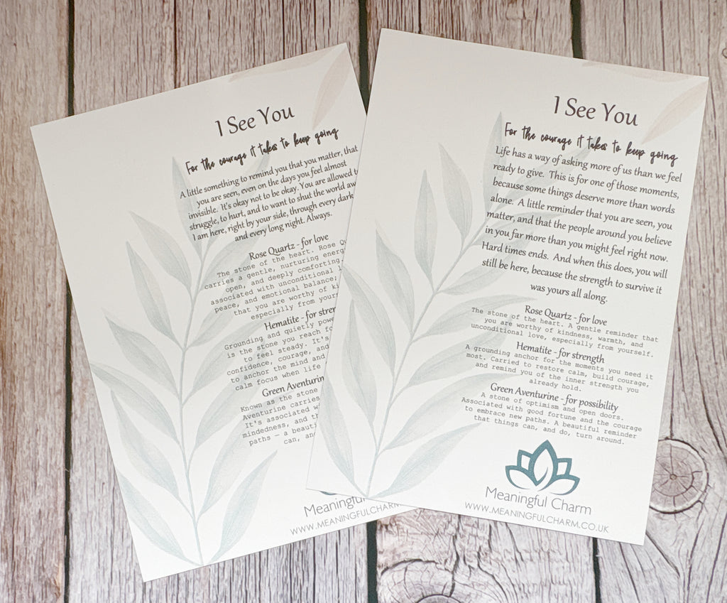 Two printed cards with inspirational poetry titled 'I See You' laid on a rustic wood surface. The cards are off-white with gray botanical leaf illustrations and black text, and the brand name Meaningful Charm is visible at the bottom.