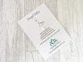 Angel Baby charm on a card with text and branding on a wooden surface