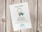 Keychain with angel wings and heart on a Meaningful Charm card on a wooden surface
