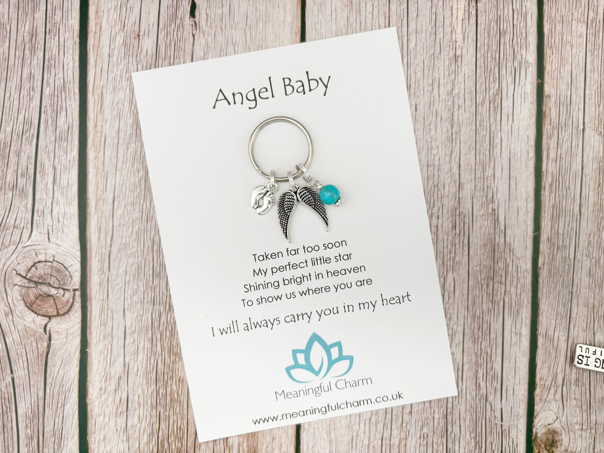 Keychain with angel wings and heart on a Meaningful Charm card on a wooden surface