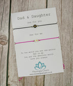 Two bracelets with cards for 'Dad & Daughter' on a wooden surface.