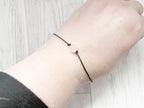 Close-up of a wrist wearing a black bracelet with a pink bead on a light wooden surface.