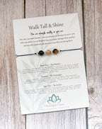 A beaded black cord bracelet with three beads (black, brown, and cream) displayed on its printed backing card, which features inspirational quotes and product descriptions for 'Meaningful Charm'.