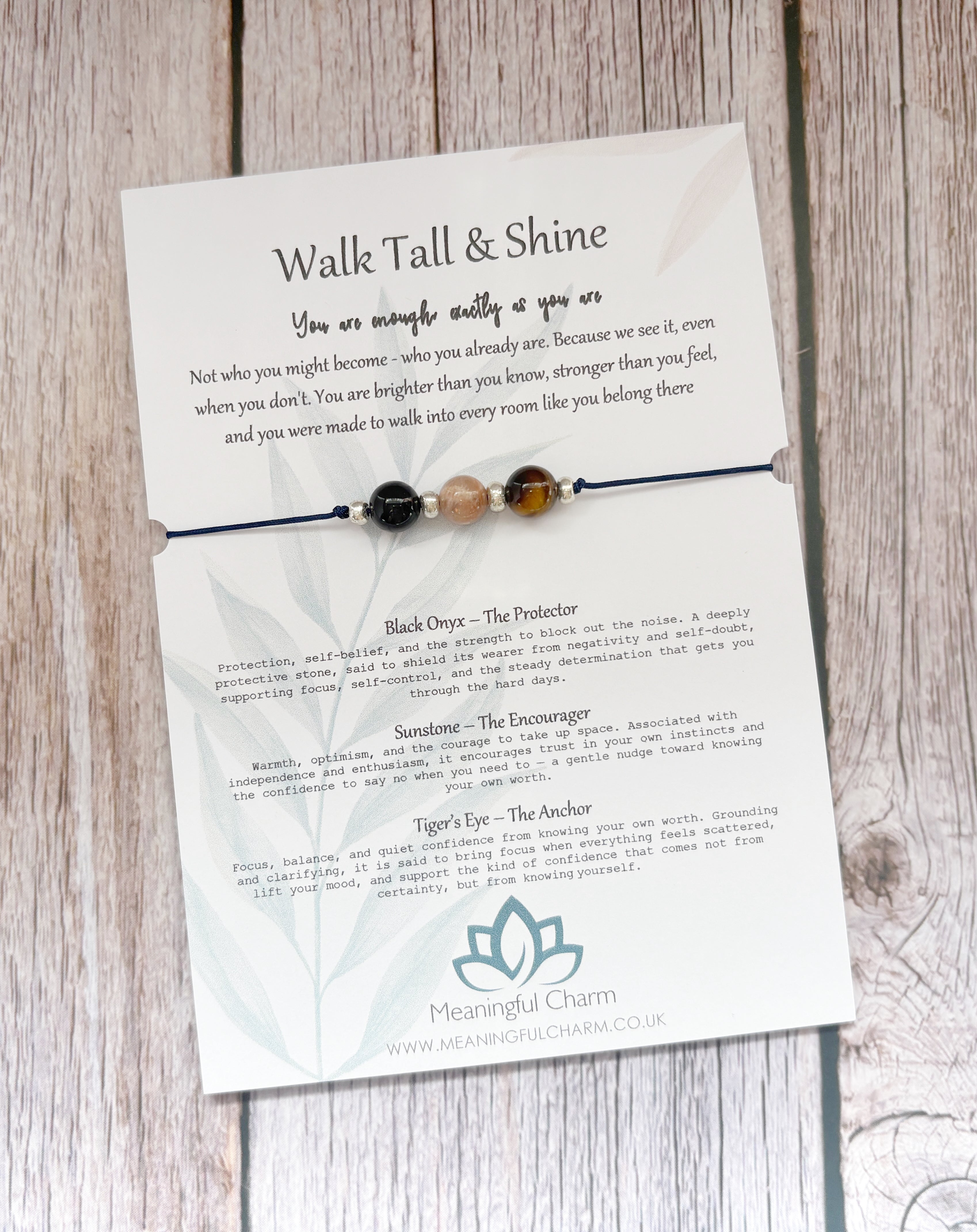 A beaded black cord bracelet with three beads (black, brown, and cream) displayed on its printed backing card, which features inspirational quotes and product descriptions for 'Meaningful Charm'.