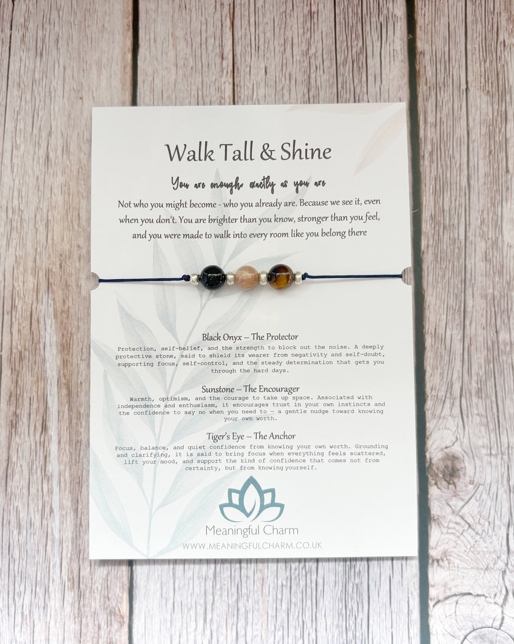 A beaded spiritual necklace with black, white, and brown beads displayed on its printed backing card, which reads 'Walk Tall & Shine' and features descriptions for the beads and meanings, set against a light wood background.