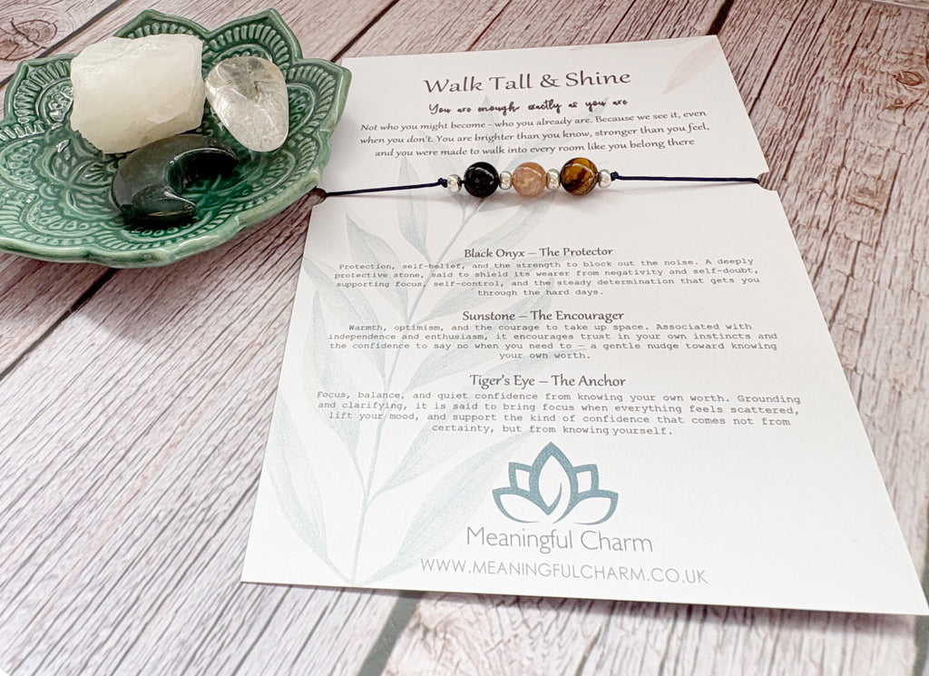 A printed card set from Meaningful Charm titled 'Walk Tall & Shine' laid on a whitewashed wood surface, alongside a green ceramic dish holding crystals and a small beaded bracelet.