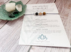 A printed card set from Meaningful Charm laid out on a whitewashed wood surface, including a 'Walk Tall & Shine' affirmation card, a matching card with three gemstone beads, and a green ceramic dish holding a white candle and clear crystals.